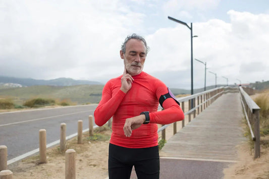 Älterer Mann in roter Sportkleidung misst seinen Puls während eines Lauftrainings auf einer Promenade.