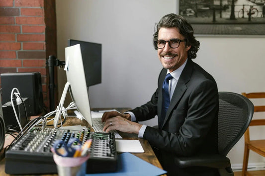 Freundlich lächelnder Mann im Anzug mit Brille arbeitet an einem Computer in einem modern eingerichteten Büro.