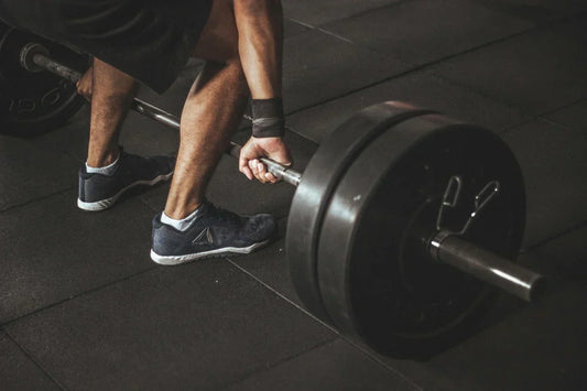 Nahaufnahme eines Athleten beim Kreuzheben mit einer schweren Langhantel im Fitnessstudio.