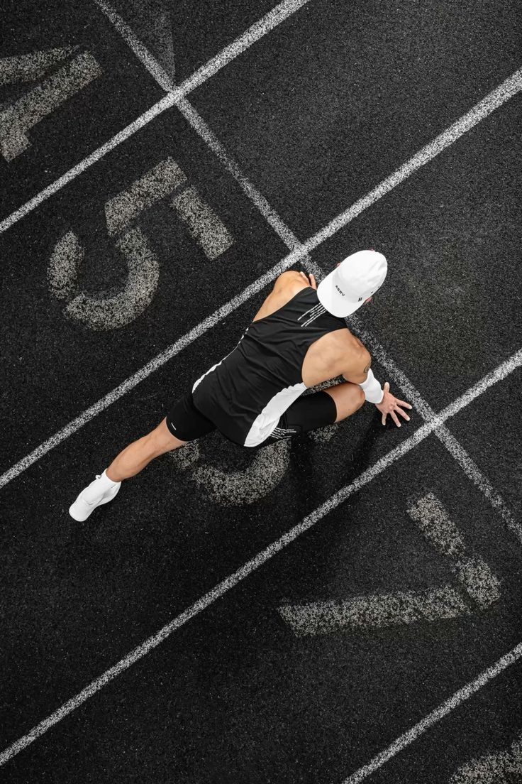 Athlet in schwarzer Sportkleidung startet aus dem Startblock auf einer Laufbahn, Draufsicht von oben, Fokus auf Wettkampf und Sprintbeginn.